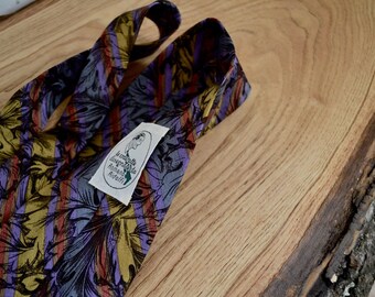 Puede incluir: Una corbata de seda a rayas de color morado, dorado y rojo con un patrón de hojas. La corbata tiene una etiqueta que dice "La cravatta Italiana Handmade in Italy".