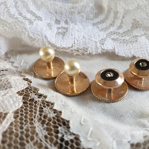 Può includere: Quattro gemelli d'oro con dettagli in perla e nero. Due gemelli hanno una parte superiore in perla e due gemelli hanno un centro nero con un bordo dorato.