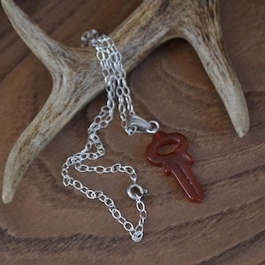 May include: A silver chain necklace with a carnelian key pendant. The key is a deep reddish-brown color and has a detailed design.