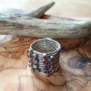 May include: A silver ring with multiple bands and red and yellow gemstones. The ring is on a wooden surface.