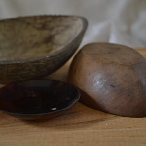May include: Three wooden bowls of varying sizes and shapes. The largest bowl is light brown and has a rough texture. The medium bowl is dark brown and has a smooth texture. The smallest bowl is dark brown and has a smooth, shiny surface.