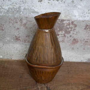 Puede incluir: Un jarrón de cobre con acabado martillado. El jarrón tiene una boca ancha y una base estrecha. Es una pieza única y decorativa.