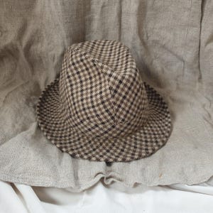 Peut inclure: Un chapeau fedora en tissu à carreaux marrons et beiges.