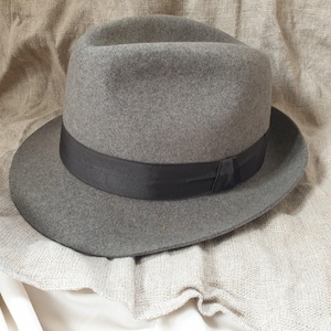 May include: A gray fedora hat with a black band. The hat is made of felt and has a classic style.