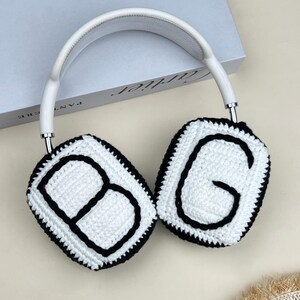 Peut inclure: Casque audio blanc et argent&eacute; avec des coussinets d'oreille en crochet. Les coussinets sont blancs avec des contours noirs et les lettres "BG" au centre. L'arceau est blanc avec un d&eacute;tail en m&eacute;tal argent&eacute;.