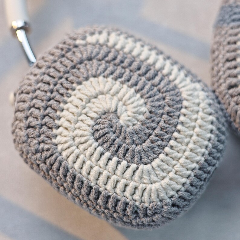 May include: Grey and white crocheted earmuffs with a circular pattern.