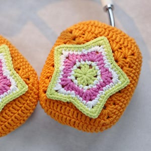 May include: Two crocheted orange headphone covers with a star-shaped design in pink, green, and white.