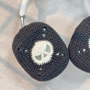 May include: A pair of black and white crocheted headphone covers with a white flower design in the center.
