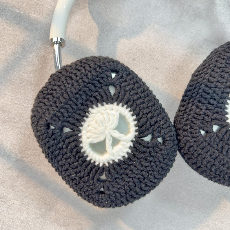 May include: A pair of black and white crocheted headphone covers with a white flower design in the center.