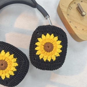 May include: Black headphones with crocheted sunflower ear covers. The ear covers are black with a yellow sunflower design.