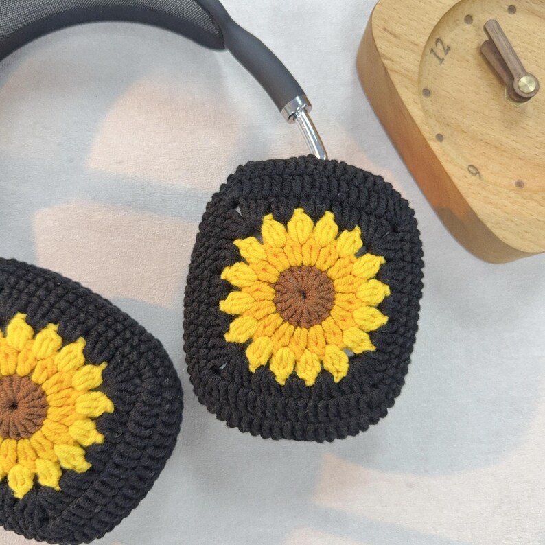 May include: Black headphones with crocheted sunflower ear covers. The ear covers are black with a yellow sunflower design.