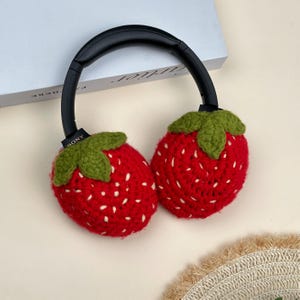 May include: Headphones with red strawberry-shaped ear covers. The ear covers are crocheted with white seed details and green leaf tops. The black headband has the brand name "SONY" printed on the side.