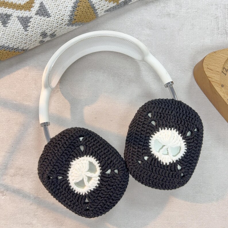 May include: White headphones with black and white crocheted ear covers. The ear covers have a white circle in the center with a flower design.