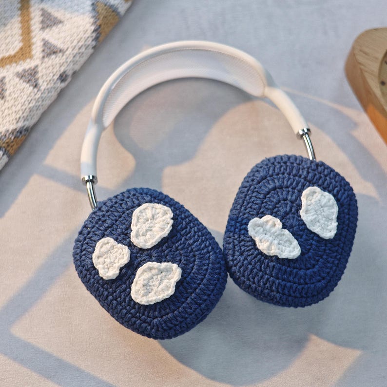 May include: Blue crocheted ear warmers with white cloud designs. The ear warmers are attached to a white headband.