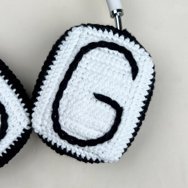 Peut inclure: Caches d'&eacute;couteurs en crochet blanc avec un contour noir et la lettre "G" noire au centre. Les bords sont &eacute;galement soulign&eacute;s en noir. Le casque est blanc.