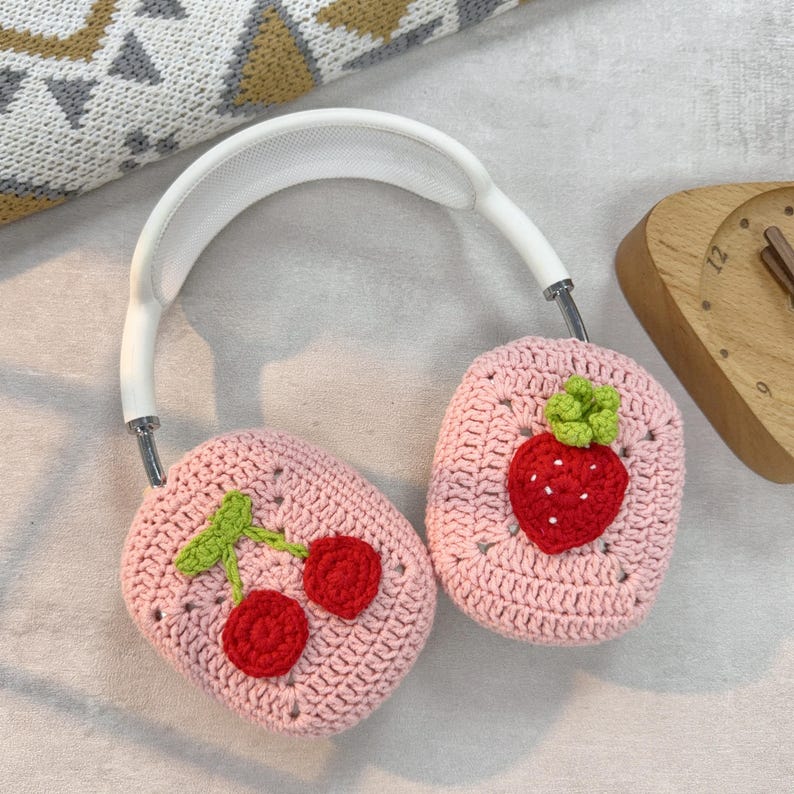 May include: White headphones with pink crocheted earmuffs. One earmuff has a crocheted strawberry design, the other has a crocheted cherry design.