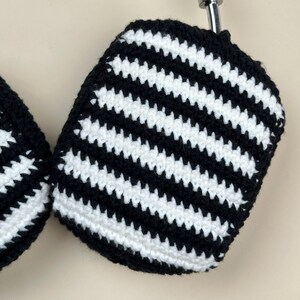 May include: Close-up of a pair of black and white striped crochet ear covers. The ear covers are made of a soft yarn and have a repeating pattern of black and white horizontal stripes. The ear covers are designed to fit over headphones.