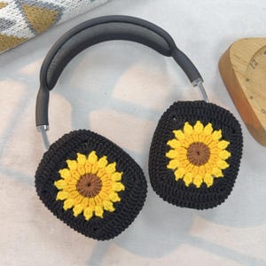 May include: Black headphones with crocheted sunflower ear covers. The ear covers are black with a yellow sunflower design.