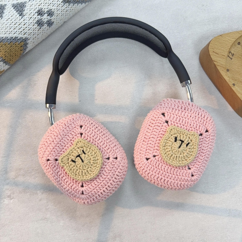 May include: Pink crocheted headphone covers with a brown crocheted bear face on each cover.