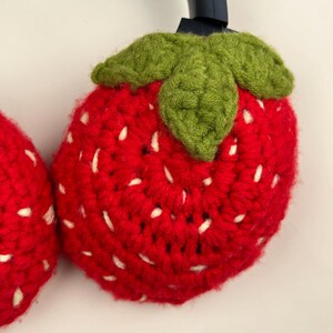 May include: Crocheted strawberry headphone covers. The red covers have white seed details and green leaf accents. The handmade covers are designed to fit over the ear cups of headphones. The strawberry design adds a playful touch to the headphones.