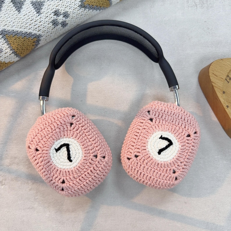 K&ouml;nnte beinhalten: Rosa gestrickte Kopfh&ouml;rerbez&uuml;ge mit einem wei&szlig;en Kreis und der Zahl "7" auf jedem Bezug.