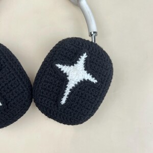 May include: Black crochet headphone covers with a white star design. The covers are designed to fit over the earcups of headphones. The headphones have a white headband.