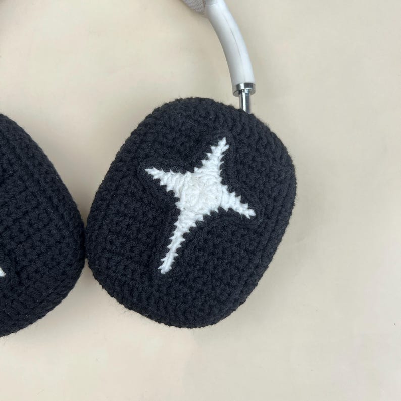 May include: Black crochet headphone covers with a white star design. The covers are designed to fit over the earcups of headphones. The headphones have a white headband.