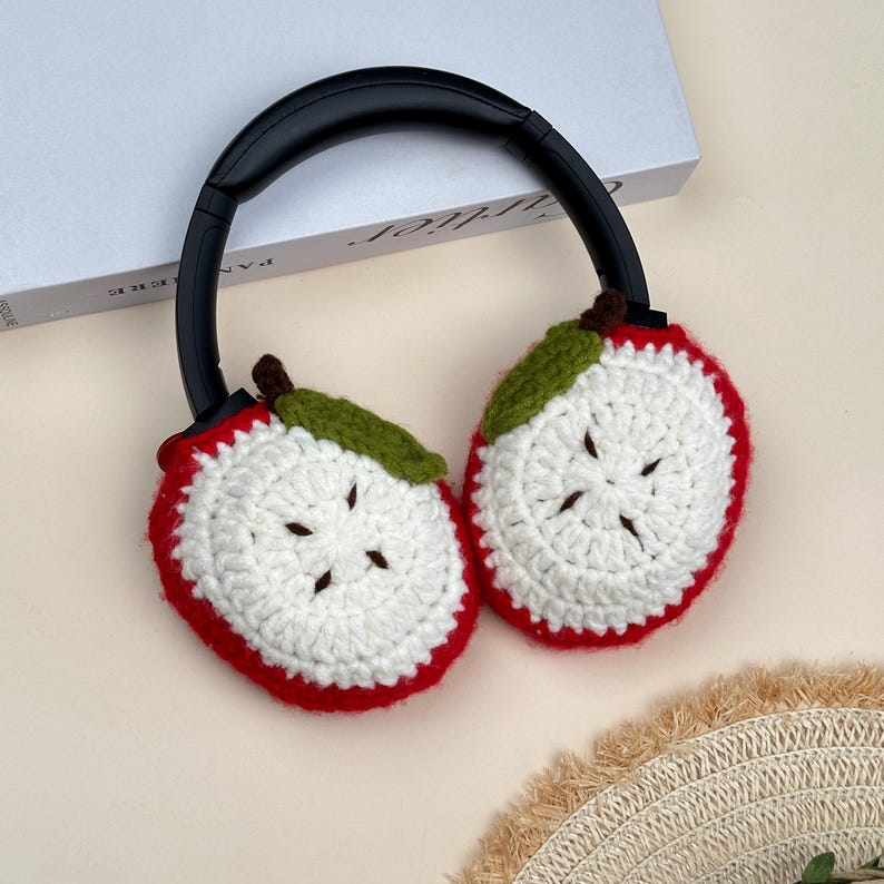 Puede incluir: Auriculares de crochet con cubiertas para los o&iacute;dos en forma de rodajas de manzana. Las cubiertas para los o&iacute;dos son blancas con bordes rojos, hojas verdes y tallos marrones. Los auriculares tienen una diadema negra.