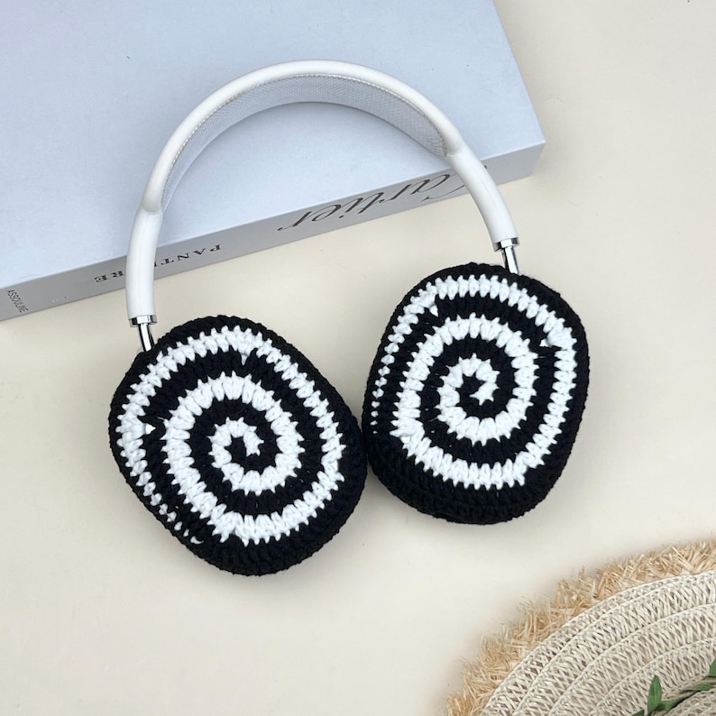 Pode incluir: Fones de ouvido brancos e prateados com capas de ouvido de croch&ecirc; em espiral preto e branco. Os fones de ouvido t&ecirc;m uma faixa de cabe&ccedil;a branca e detalhes prateados. As capas de ouvido s&atilde;o pretas com um design em espiral branco.