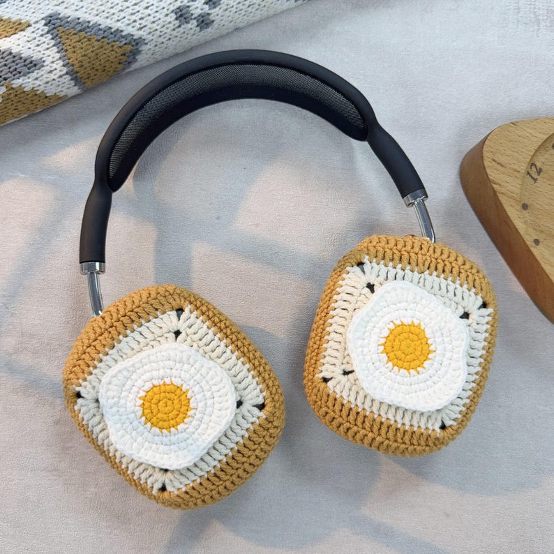 May include: A pair of headphones with crocheted covers shaped like fried eggs. The covers are brown, white, and yellow.