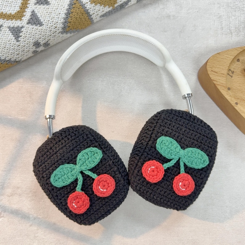 Pu&ograve; includere: Copri auricolari in maglia nera con un design a ciliegie. Le ciliegie sono rosse con steli e foglie verdi.