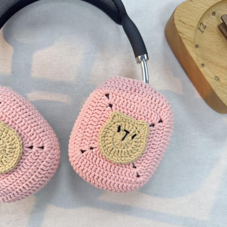 May include: Pink crocheted headphone covers with a brown crocheted cat face on each cover.