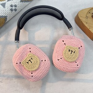 May include: Pink crocheted headphone covers with a brown crocheted bear face on each cover.