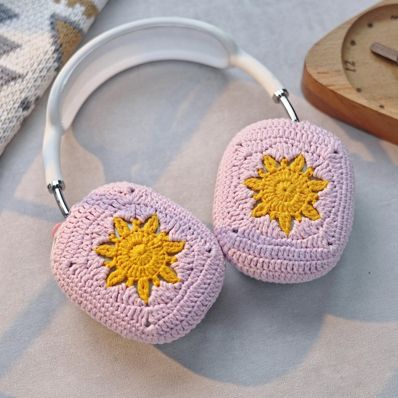 K&ouml;nnte beinhalten: Ein Paar rosa geh&auml;kelte Ohrensch&uuml;tzer mit gelben geh&auml;kelten Blumendesigns. Die Ohrensch&uuml;tzer sind an einem wei&szlig;en Stirnband befestigt.