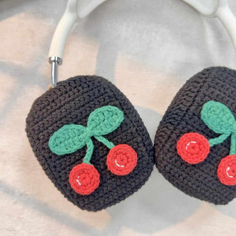 Pu&ograve; includere: Copri auricolari in crochet nero con un design a ciliegie. Le ciliegie sono rosse con foglie verdi.