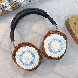 May include: Brown and white crocheted headphone covers with a blue and white circle pattern. The covers are on a pair of black headphones.