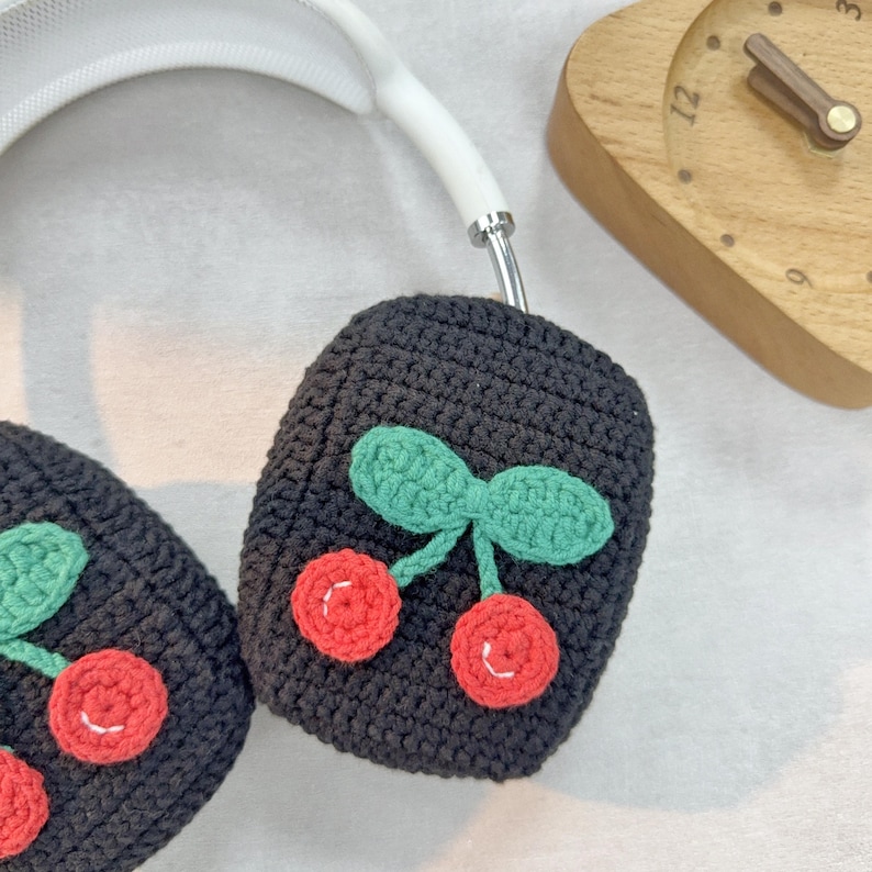 Pu&ograve; includere: Copri cuffie in crochet nero con un design a ciliegie. Le ciliegie sono rosse con foglie verdi.