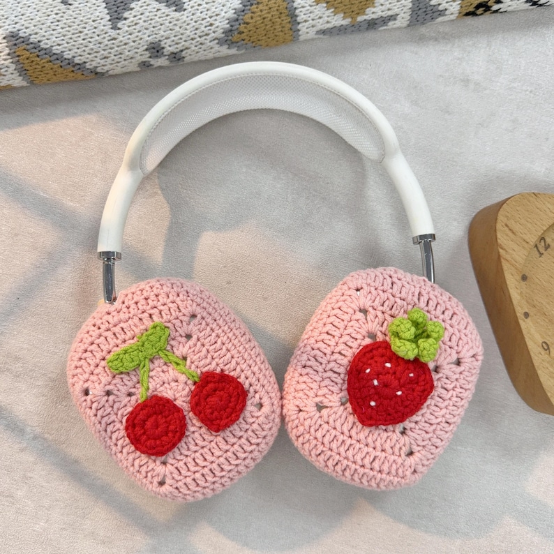 May include: Pink crocheted headphone covers with a strawberry and cherry design. The covers are made of soft yarn and are perfect for protecting your headphones from scratches and dirt.