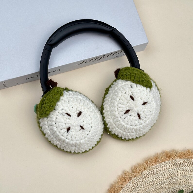 Puede incluir: Auriculares negros con cubiertas para los o&iacute;dos de ganchillo blancas y verdes. Las cubiertas para los o&iacute;dos est&aacute;n dise&ntilde;adas para parecerse a fruta en rodajas, con centros blancos y c&aacute;scaras verdes. Los auriculares est&aacute;n sobre una superficie blanca.