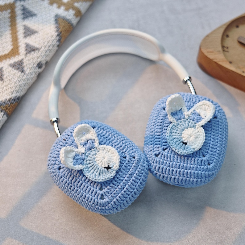 May include: Blue crocheted ear warmers with a white bunny design. The ear warmers are attached to a white headband.