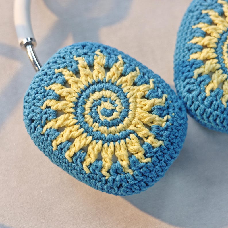 May include: A pair of blue crocheted headphone covers with a yellow crocheted sun design.