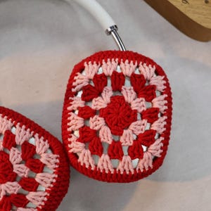 Pode incluir: Protetores de ouvido de croch&ecirc; vermelhos e rosados para fones de ouvido. Os protetores de ouvido s&atilde;o feitos com um padr&atilde;o de granny square.