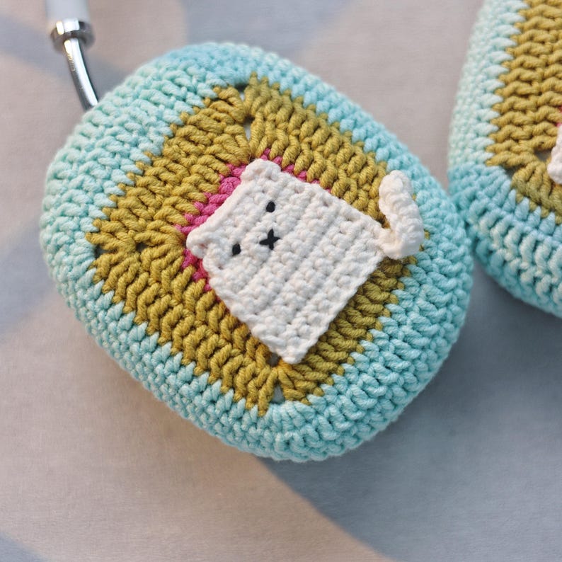 May include: A crocheted teal and yellow airpod case with a white crocheted cat design.