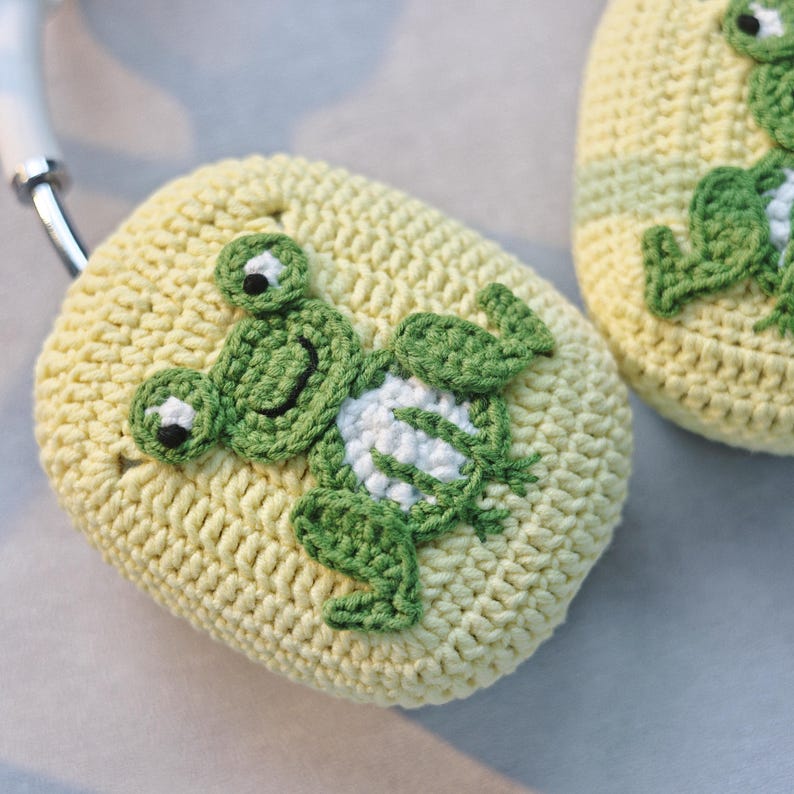 May include: A pair of yellow crocheted headphone covers with green frog appliques. The frogs have white accents and black eyes.