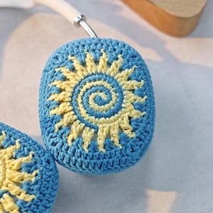 May include: A pair of blue crocheted headphone covers with a yellow sun design.