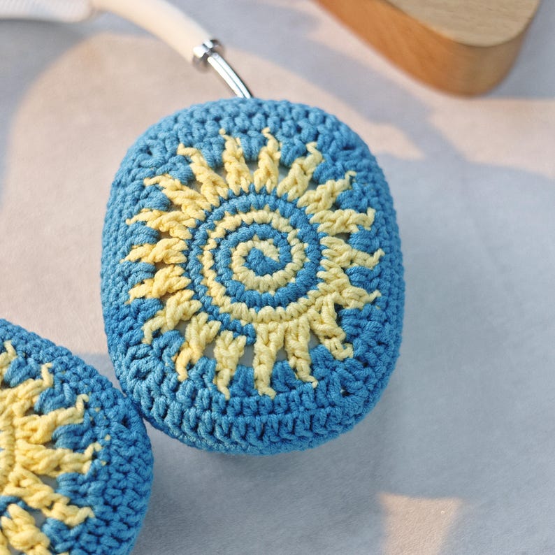 May include: A pair of blue crocheted headphone covers with a yellow sun design.
