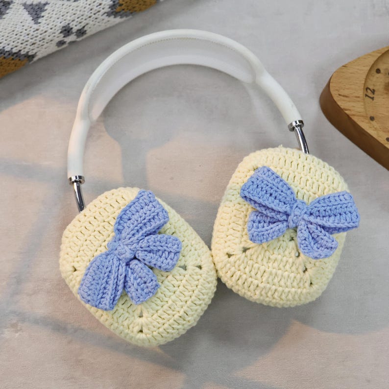 May include: A pair of crocheted ear warmers with a light yellow base and blue bow accents. The ear warmers are attached to a white headband.