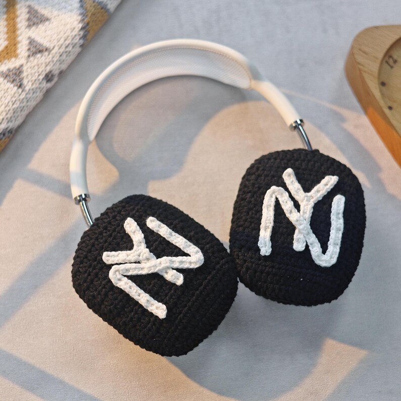May include: Black crocheted earmuffs with white "NY" lettering on each earcup. The earmuffs are attached to a white headband.