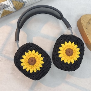 May include: Black headphones with crocheted sunflower earmuffs. The earmuffs are black with a yellow sunflower design.