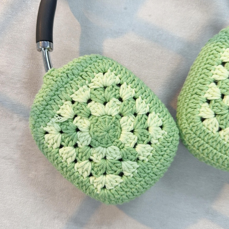 Op de afbeelding: Groene gehaakte oorkappen met een granny square patroon. De oorkappen zijn gemaakt met een lichtgroen garen en een donkergroen garen.